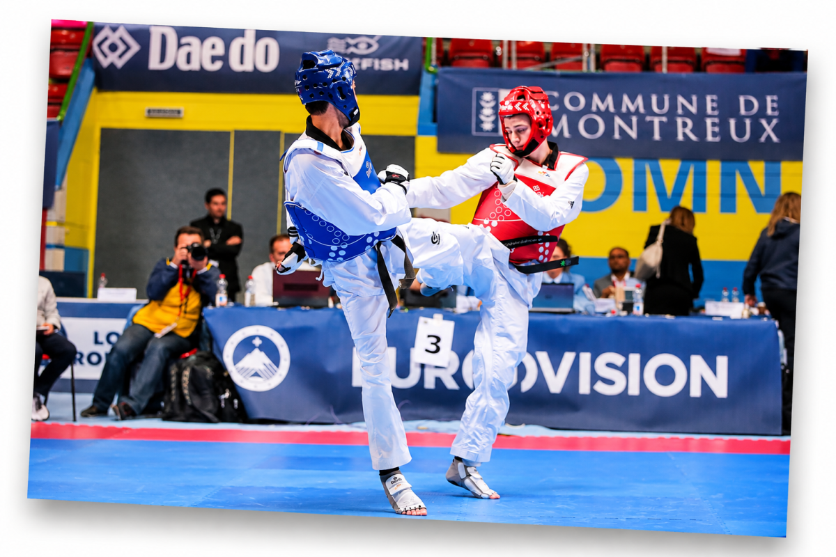 Two athletes competing on the mat at the 2016 European Taekwondo Championships in Montreux, one wearing blue protective equipment and the other red, in front of competition officials.